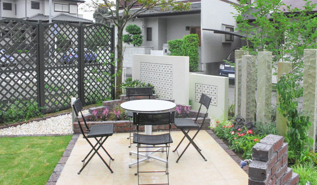 砂岩の石柱のフェンスと緑に囲まれたタイルテラス